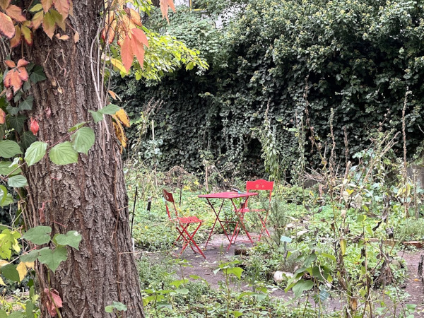 cafe botanico zwei rote Gartenstühle mit einem kleinen Bistrotisch in einem Naturgarten